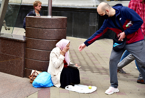 A man gives money to a homeless elderly woman. Grandma begs for alms. Old woman begging on the street. Homeless beggar asking for help. Social problem. risis concept. Russia, Moscow, JUN 07, 2020