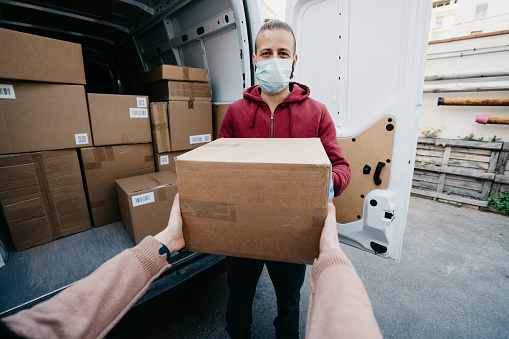 Pov view of a woman receiving a parcel from a delivery man. The man is wearing a protective face mask.