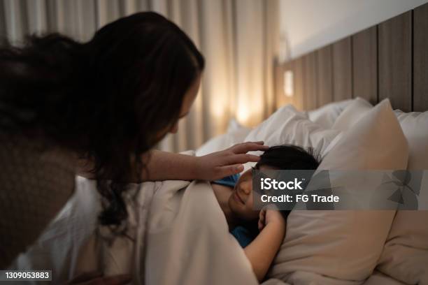 Mother Tucking Daughter Into Bed At Night Stock Photo - Download Image Now - Child, Bedtime, Mother
