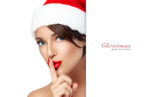 Christmas Woman in Santa Hat doing a Hush Sign Christmas woman. Beauty model girl in Santa Claus hat with red lips and matching manicure doing a hush sign. Closeup portrait isolated on white background with copy space for text santa claus expressions shhh stock pictures, royalty-free photos & images