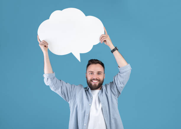 istock Millennial hipster guy holding speech bubble on blue studio background, mockup for design 1309054693