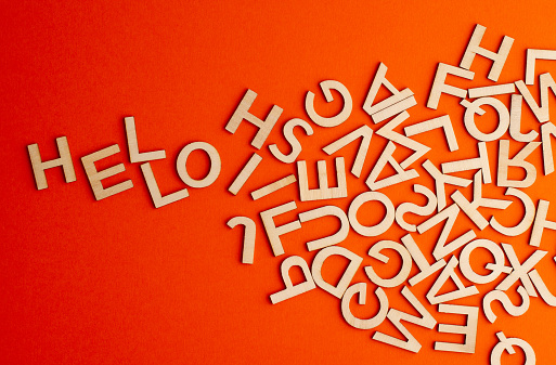 top view closeup detail macro of many wooden cut small alphabet letters on orange background spelling the word hello