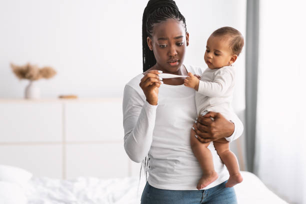 spaventata giovane madre afroamericana che guarda il termometro - child fever illness thermometer foto e immagini stock