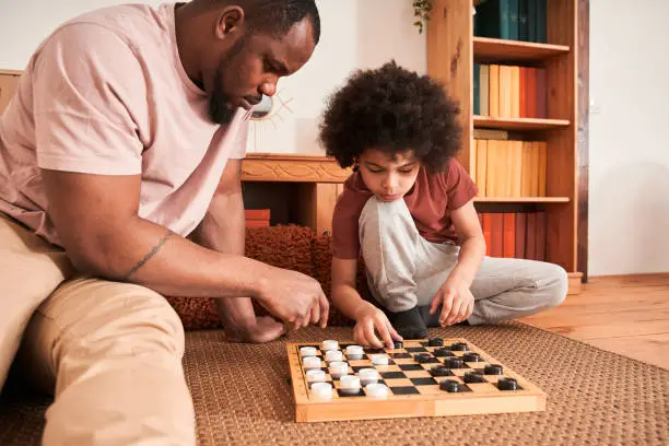 Photo of Boy sitting in front of his father and playing at checkers