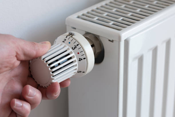 person turning down thermostat on heater to save energy stock photo