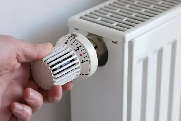 close-up of person turning down thermostat on heater to save energy