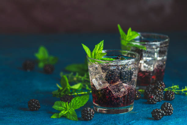 Cold summer berry drink with blackberries. Refreshing summer drink with syrup, blackberry and ice on dark blue concrete background stock photo