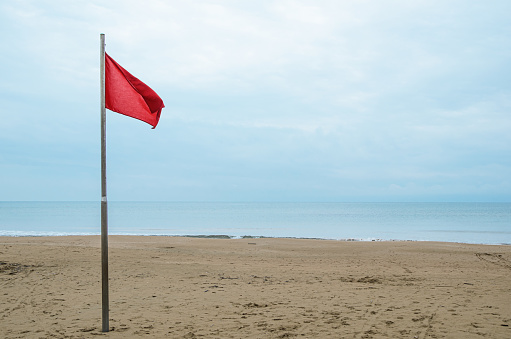 Empty sandy beach and red storm flag on a cloudy day. Security on public and private beaches, storm alert system.