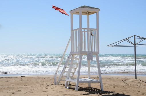 Empty lifeguard tower and red storm flag on the beach in stormy weather. Lack of lifeguards on the beach during the non-tourist season. Security on public and private beaches, storm alert system.