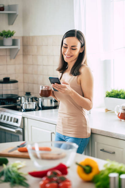 istock Modern happy young cute woman relaxing while using her smart phone in the kitchen at home 1309073403