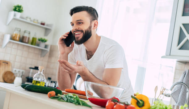 istock Happy handsome bearded man is using his smart phone while he preparing vegan healthy breakfast for a lovely family 1309073555