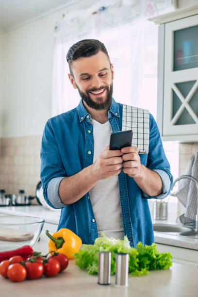 istock Happy handsome bearded man is using his smart phone while he preparing vegan healthy breakfast for a lovely family 1309073632