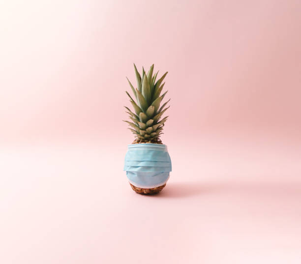 istock Blue surgical face mask on a pineapple. Pink background. Minimal concept. 1309079733