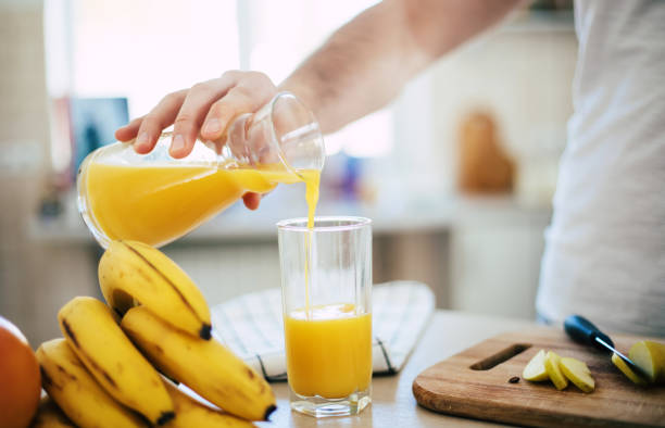 handsome young sporty smiling man in the kitchen is preparing vegan healthy fruits salad and smoothie in a good mood - blender apple banana color image imagens e fotografias de stock