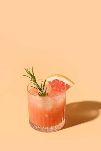 Grapefruit soda with lime garnish rosemary sprig. Mocktail Paloma. Grapefruit juice garnish rosemary sprig on color beige background. Mocktail Paloma. Close up. Vertical format. aperitif photos stock pictures, royalty-free photos & images