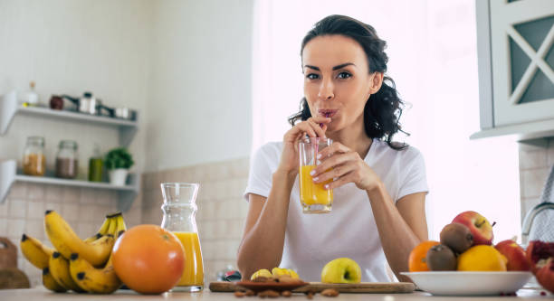 linda mujer morena joven hermosa y feliz en la cocina en casa está preparando ensalada vegana de frutas o un batido saludable y divirtiéndose - real people one person multi colored part of fotografías e imágenes de stock