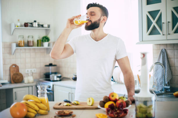 gutaussehender junger sportlich lächelnder mann in der küche bereitet vegan gesunden obstsalat und smoothie gut gelaunt zu - juicer food and drink healthy eating sport stock-fotos und bilder