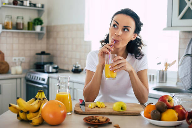 urocza piękna i szczęśliwa młoda brunetka w kuchni w domu przygotowuje owocową sałatkę wegańską lub zdrowy koktajl i dobrze się bawi - food and drink fruits and vegetables zdjęcia i obrazy z banku zdjęć