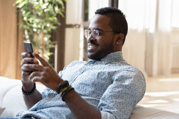istock Peaceful smiling young african man relaxing on sofa with gadget 1309082394