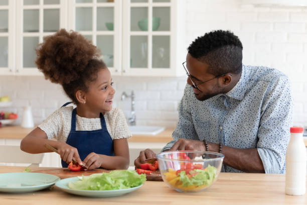 istock Pleasant african father talking with preteen daughter while cooking breakfast 1309082442