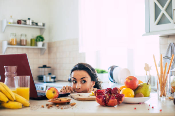 linda mujer morena joven hermosa y feliz en la cocina en casa está preparando ensalada vegana de frutas o un batido saludable y divirtiéndose - real people one person multi colored part of fotografías e imágenes de stock