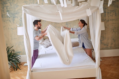 Couple making bed.Charming young couple in love making bed together.