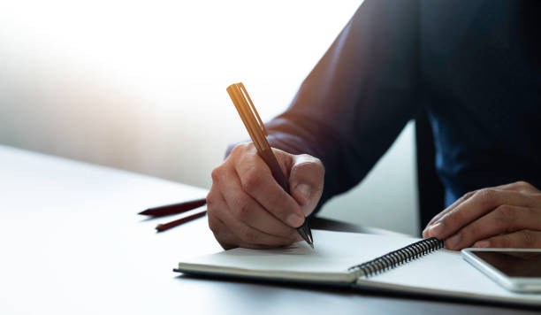istock Close-up of man hand using writing pen memo on notebook paper or letter, diary on table desk office. Workplace for student, writer with copy space. business working and learning education concept. 1309083895