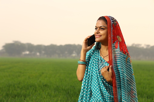 A happy rural farmer woman talking on phone happily in a Mustard field. Confident and energetic.