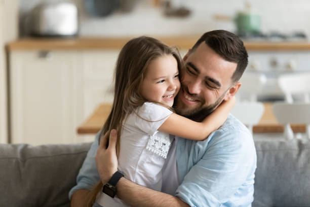 Close up smiling loving young father hugging adorable little daughter Close up smiling loving young father hugging adorable little daughter, enjoying tender moment, spending weekend together, sitting on cozy couch at home, good family relationship between dad and child daughter stock pictures, royalty-free photos & images