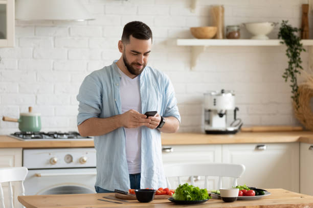 istock Young man using smartphone, cooking salad in kitchen, searching recipe 1309085653