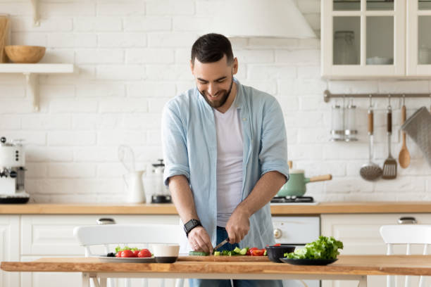 istock Smiling young man cooking salad, cutting vegetables in modern kitchen 1309085658