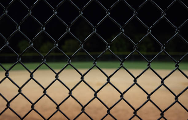 Looking through a fence at a baseball field at night.