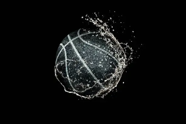 Photo of Basketball ball flying in water drops and splashes isolated on black background