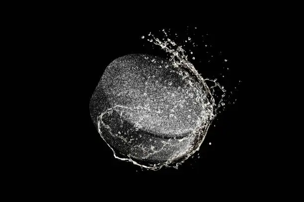 Hockey puck flying in macro water drops and splashes isolated on black background. Concept of motion, action in sport, competition, speed of game. Copyspace for ad. Highly detailed.