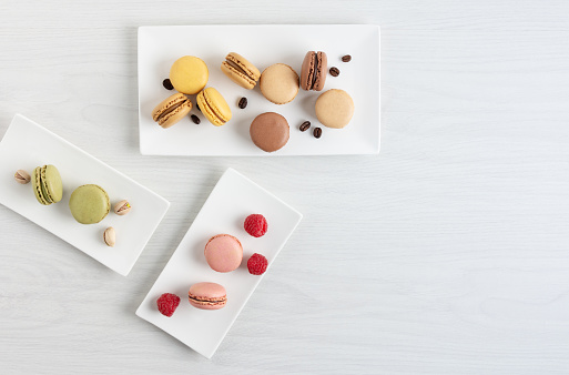 Variety of french macaroons with raspberry, coffee and pistachio on a plate on white wooden table. French meringue cookie macarons with different tastes.