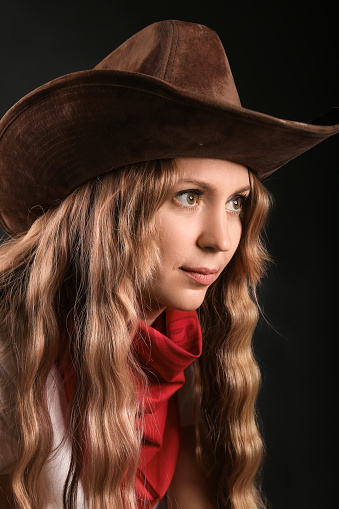 Portrait of a cowboy girl in a plaid shirt and hat. Serious sexy brutal girl of the wild west on a dark background.