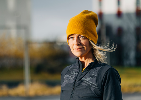 Portrait of woman outdoors wearing sportswear and knitted hat outdoors. Mature woman on a winter morning outdoors after workout.