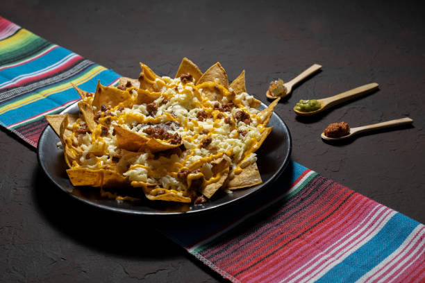 Nachos with cheese and meat on a Mexican colored fabric nachos with cheese and sauce on dark background nacho chip stock pictures, royalty-free photos & images
