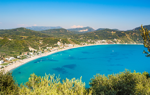 Agios Georgios beach on Corfu island in Greece. Pnoramic view of green mountains, clear sea water, secluded bay and long sandy beach. Famous destination for summer vacation tourism