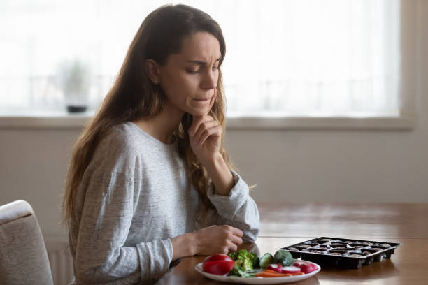 jeune femme confuse hésitant ce qu’il y a à choisir, salade ou sucreries - bon appetite photos et images de collection