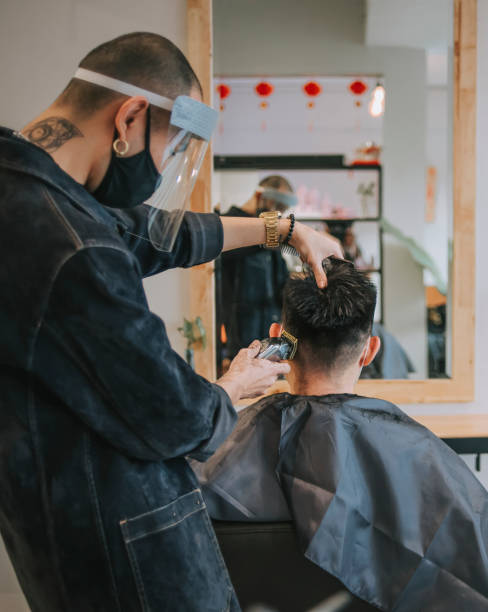 riflessione parrucchiere cinese asiatico con abbigliamento da lavoro protettivo che taglia i capelli per il suo cliente nel salone dei capelli - shaving men electric razor reflection foto e immagini stock