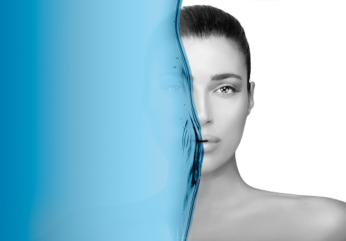 Greyscale beauty portrait of a gorgeous brunette woman. Perfect skin with no makeup makeup and half her face obscured by a blue wave in a hydration and skin care concept
