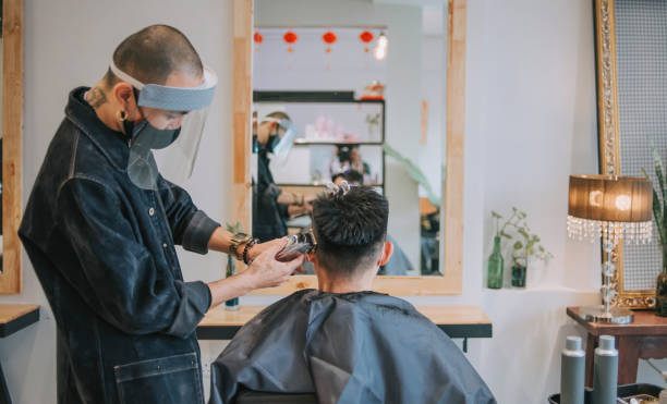 reflection asian chinese hairstylist with protective workwear cutting hair for his customer in hair saloon - shaving men electric razor reflection imagens e fotografias de stock