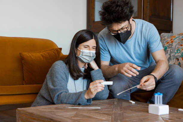 Man and woman checking the results of the Antigen Home Test for Coronavirus diagnostic. Man and woman in their 30s, wearing surgical face masks, sitting in the living room at home, checking the results of the self-swabbing Antigen Home Test for Coronavirus diagnostic. cotton swab photos stock pictures, royalty-free photos & images