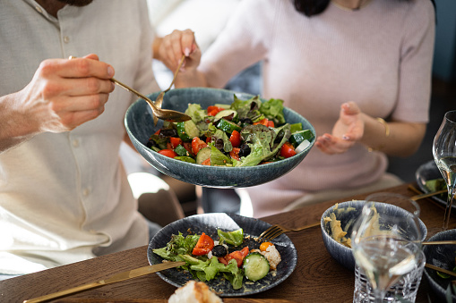 the hands of a man and a woman are holding a salad in a plate and are passing it on to each other. Lunch for two or in a company. Healthy eating.