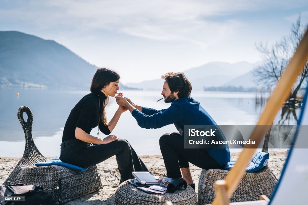 Couple smokes cbd joint by lakeshore in the morning They chat as they smoke, coastline of Lake Lugano behind Cannabis Plant Stock Photo
