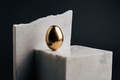 Shiny golden egg on marble cube showcase podium against black background. Luxury simple Easter holiday concept. Creative minimal success business, wealth, investments or savings composition.