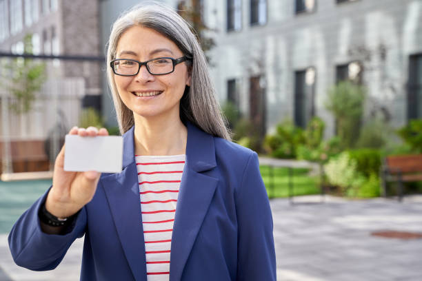 mulher de negócios madura segurando um cartão de plástico em branco e sorrindo - mature women outdoors smiling happiness - fotografias e filmes do acervo