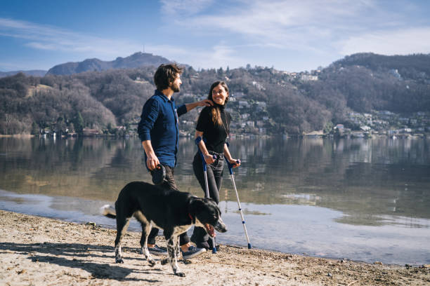 coppia a piedi con il loro cane in riva al lago al mattino - crutch foto e immagini stock