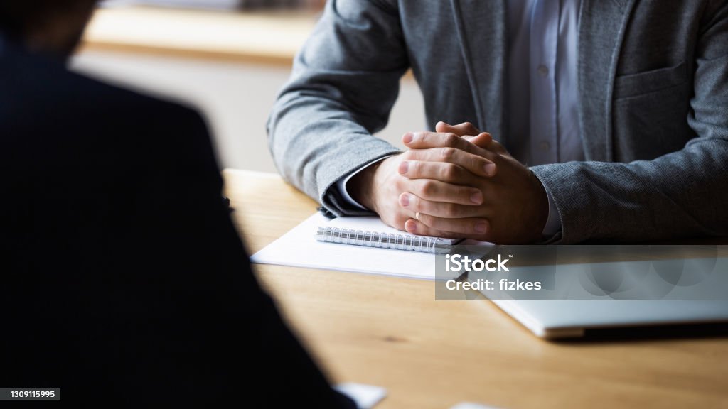 Close up focus on clasped hands of male entrepreneur. Close up focus on clasped hands of serious male entrepreneur holding negotiations meeting with partner in office. Concentrated young businessman discussing contract or agreement details with client. Interview - Event Stock Photo